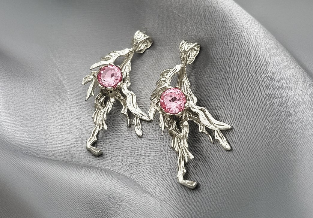 brincos de prata com pedra rosa sobre uma superfície de cetim cinza